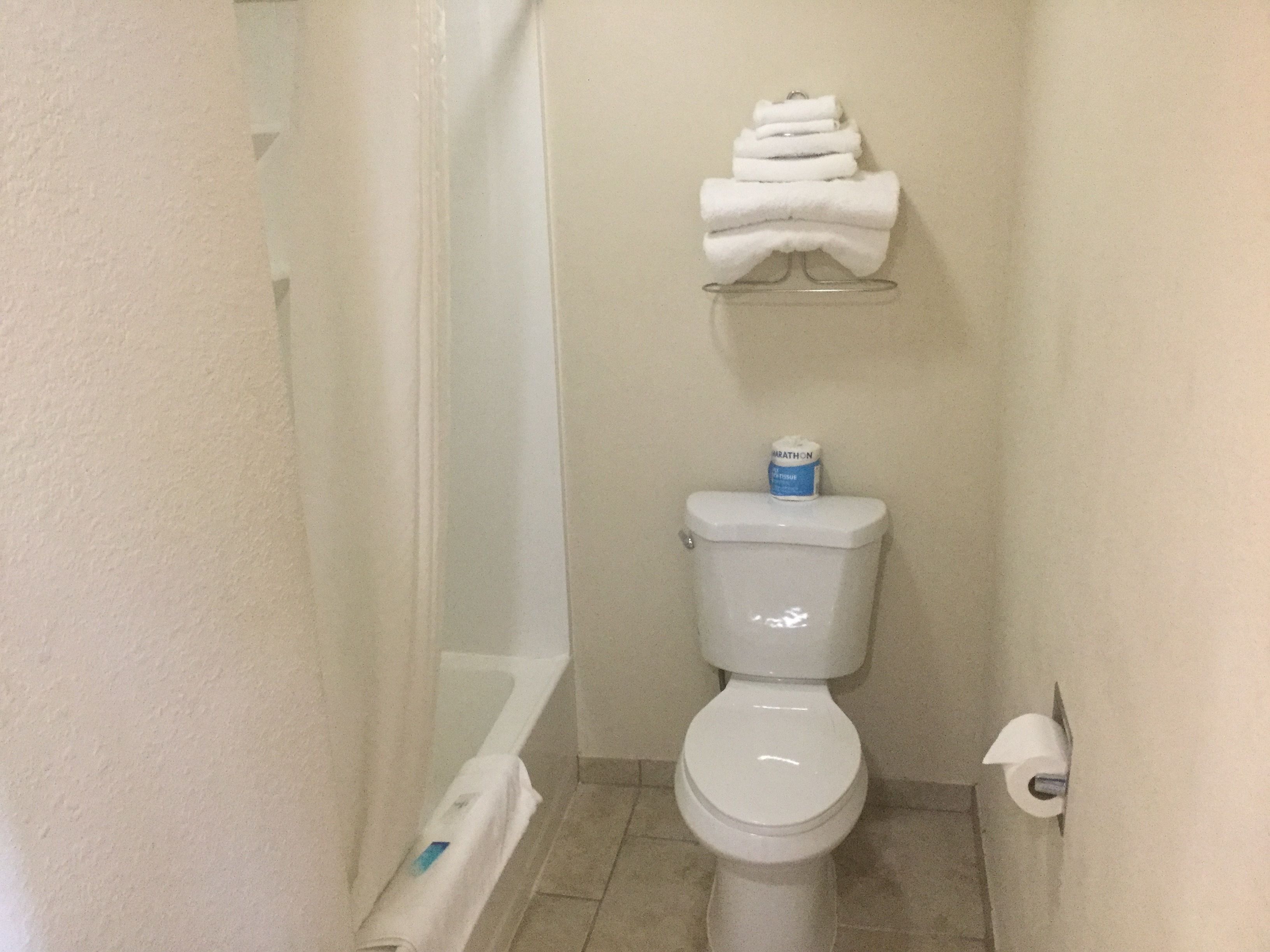 A small bathroom with a toilet, a towel rack with folded towels, and a toilet paper holder.