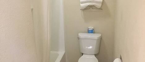 A small bathroom with a toilet, a towel rack with folded towels, and a toilet paper holder.