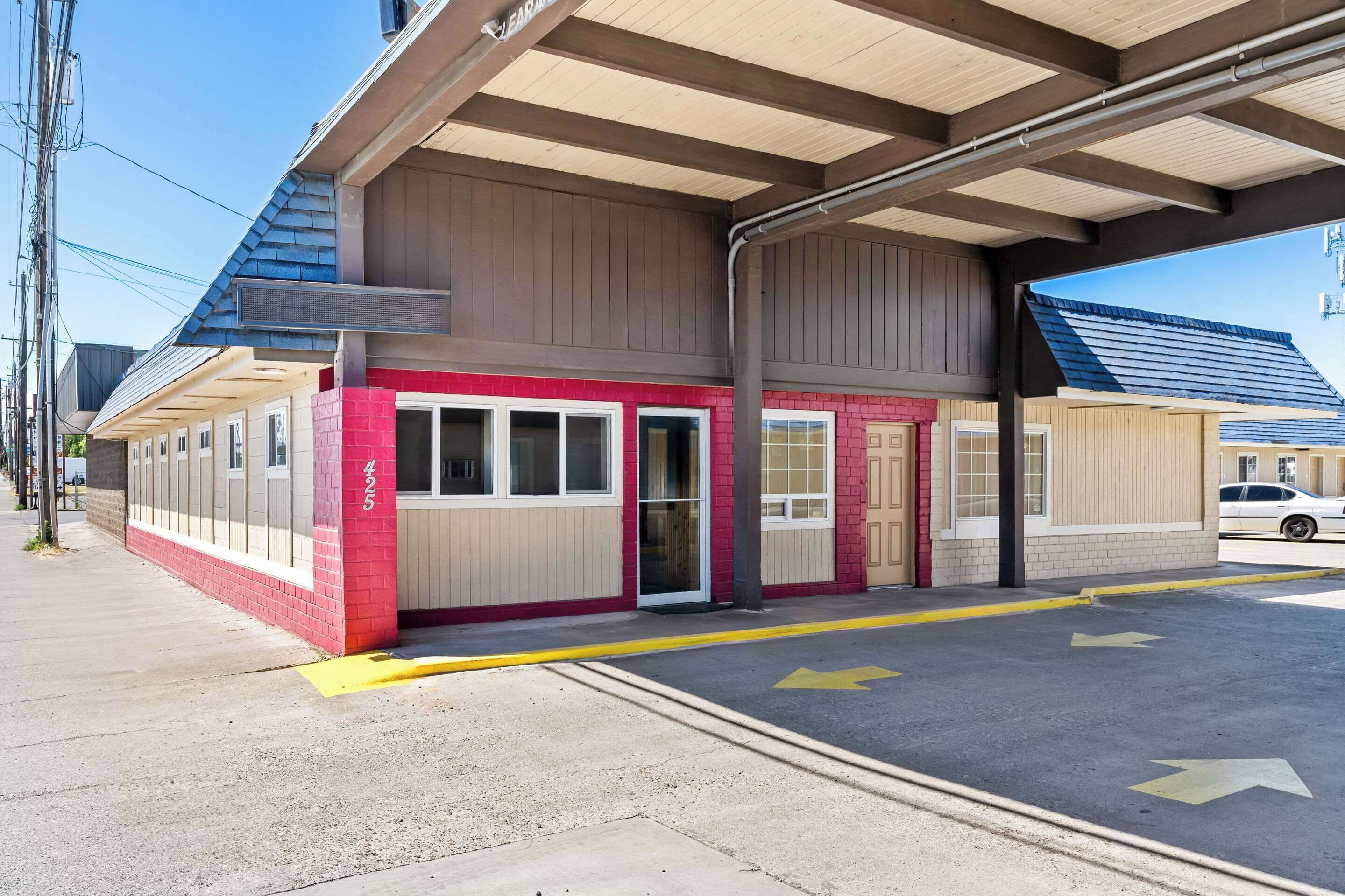 A building with a covered entrance, a red and beige facade, and a parking area with directional arrows.
