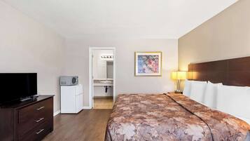 Una camera d'albergo con un letto, una TV, una cassettiera, un forno a microonde e un bagno visibile attraverso una porta aperta.
