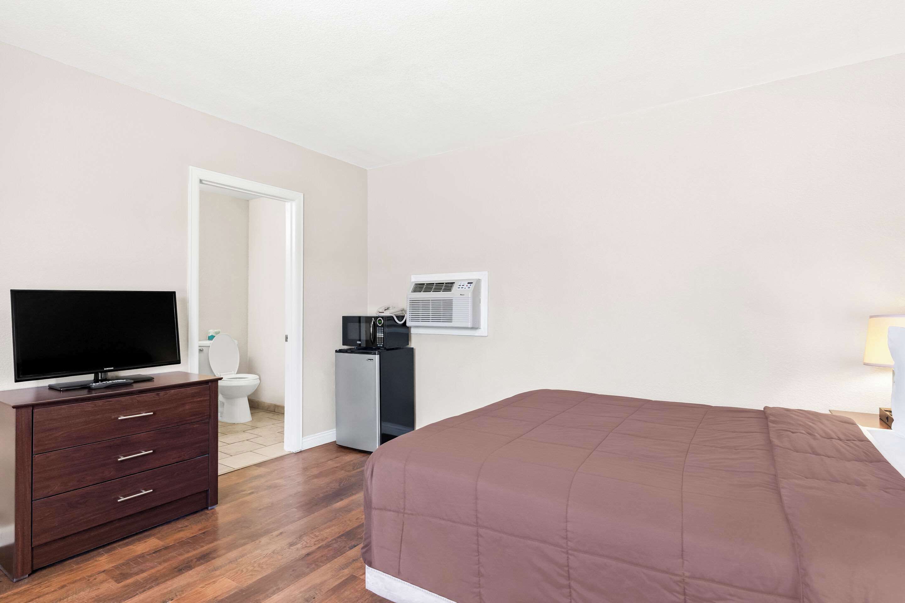 A bedroom with a bed, a TV on a dresser, a microwave, and an air conditioner.