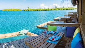 Een houten terras met zitplaatsen en een zwembad, met uitzicht op een turquoise zee met een eiland in de verte.