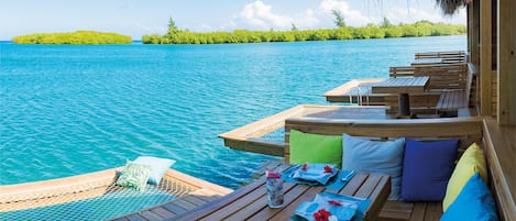 A wooden deck with seating and a pool, overlooking a turquoise sea with an island in the distance.