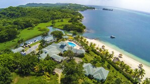 Luchtbeeld van een resort met een zwembad, strand en weelderige begroeiing.