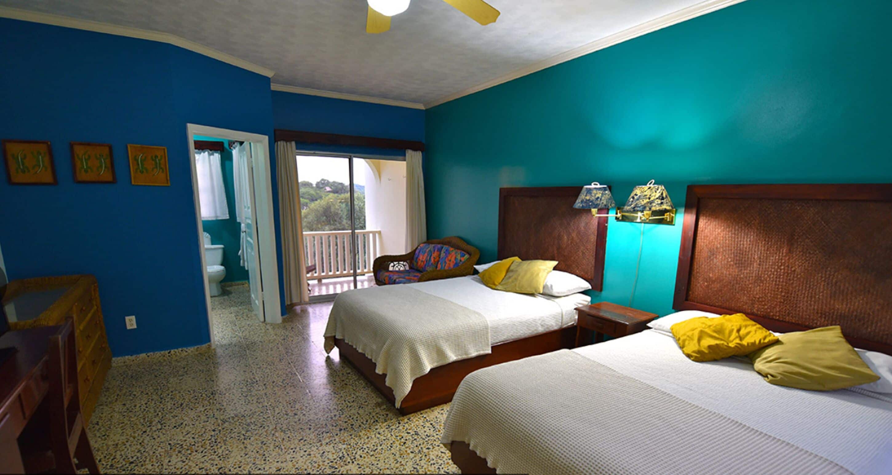 A hotel room with two beds, a balcony, and a view of the outdoors.