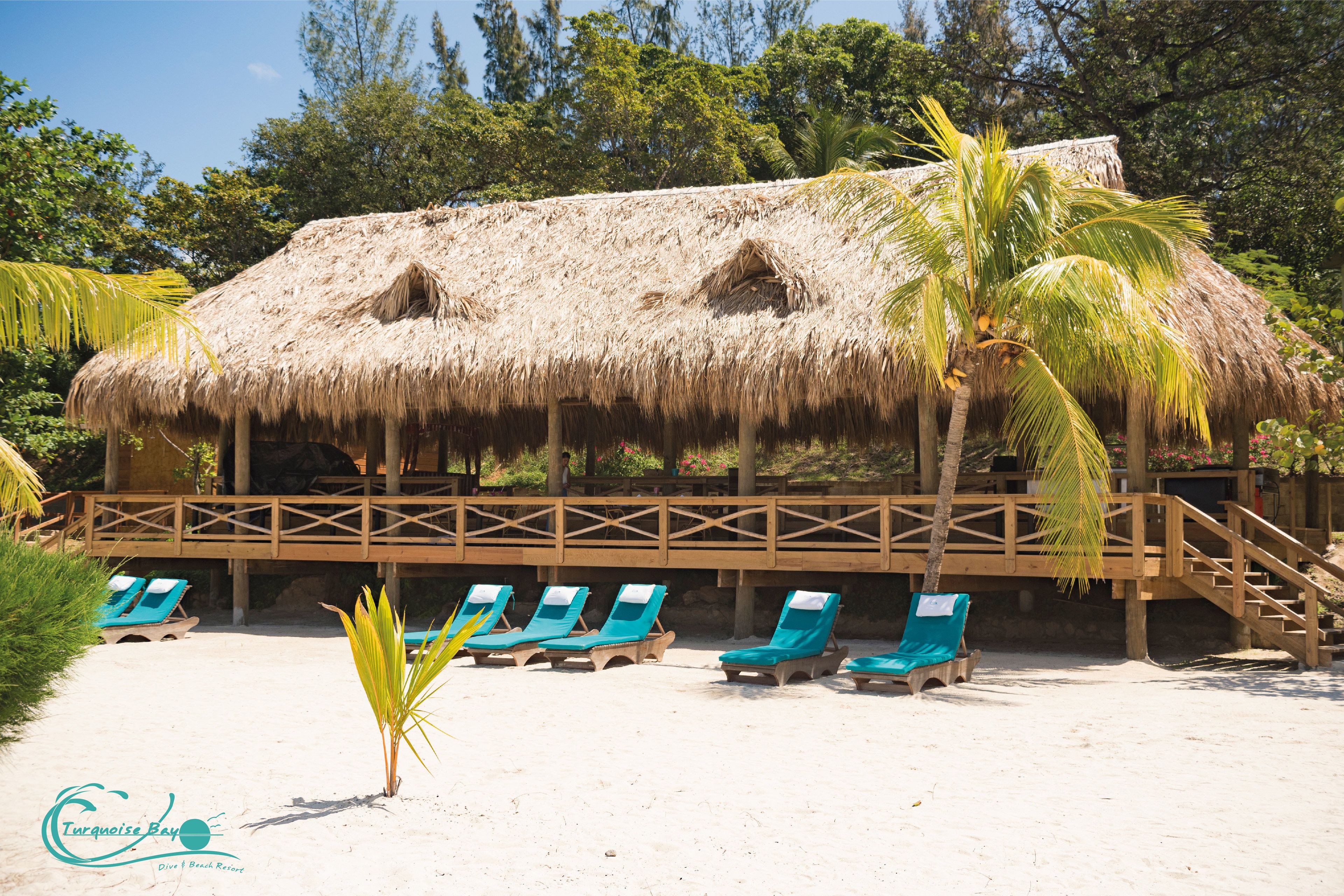 A beach hut with a thatched roof, wooden deck, and lounge chairs.