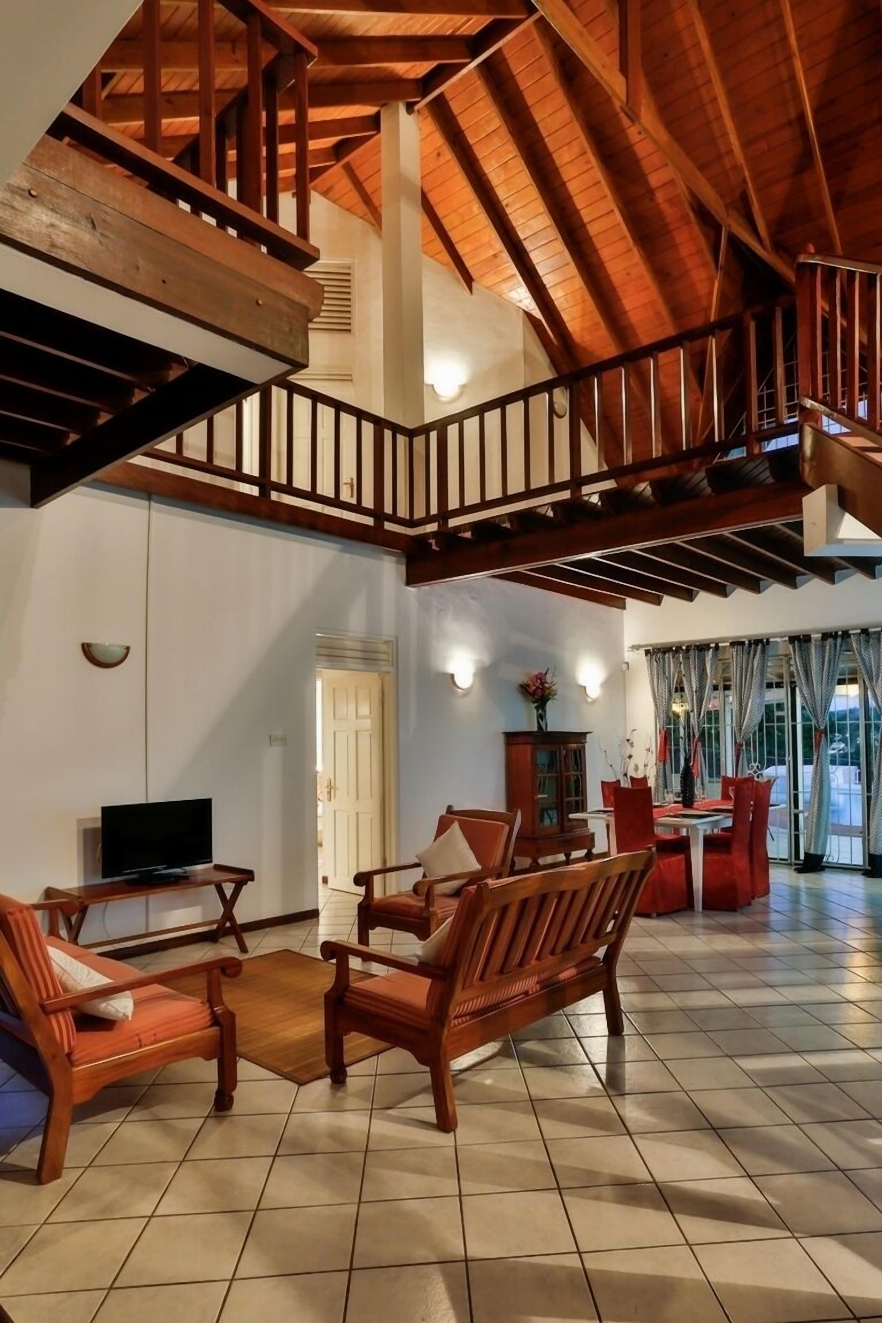A spacious living area with a high ceiling, wooden staircase, and a view of the outdoors through large windows.
