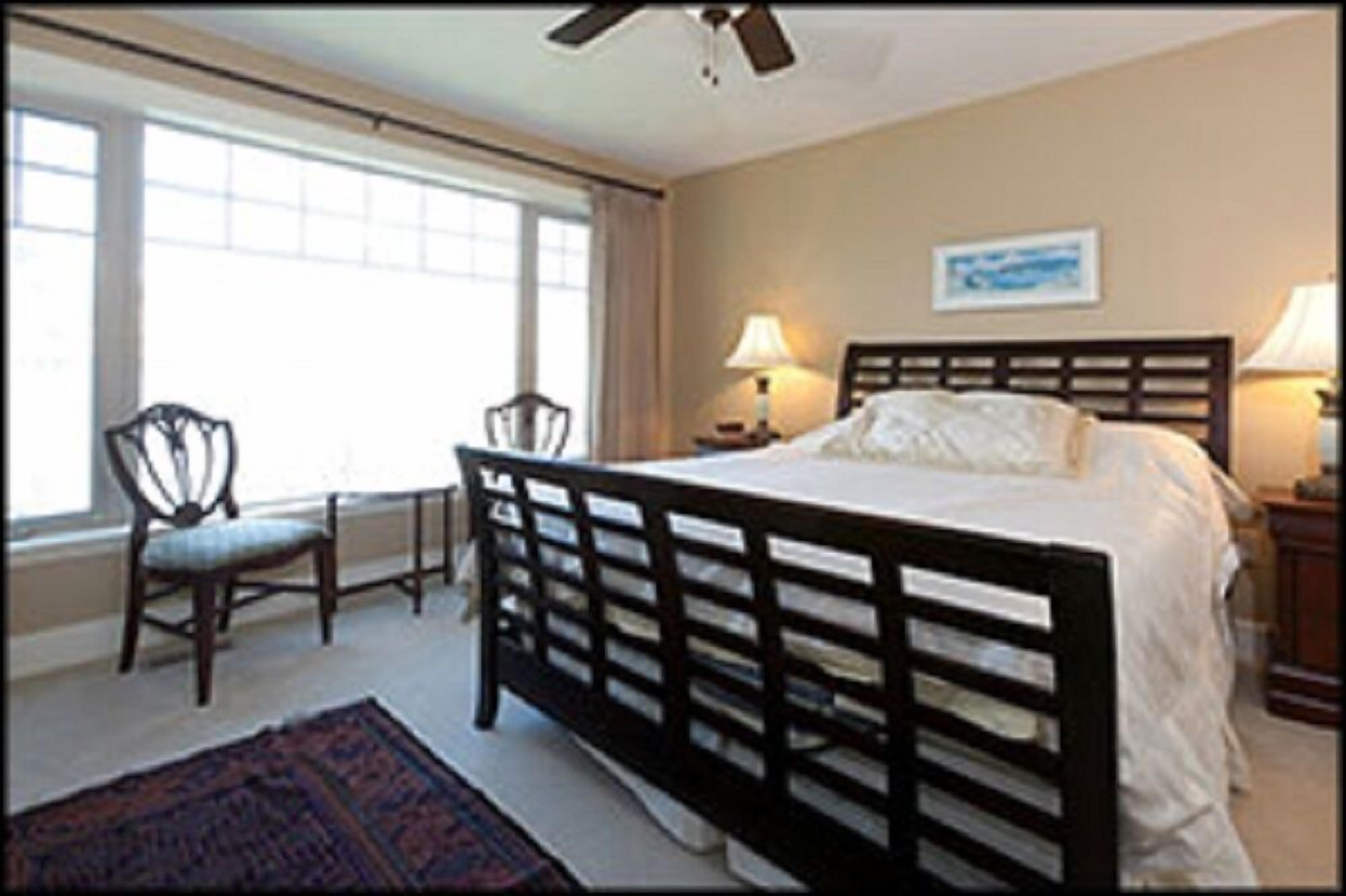 A bedroom with a large bed, two chairs, a desk, and a window with curtains.