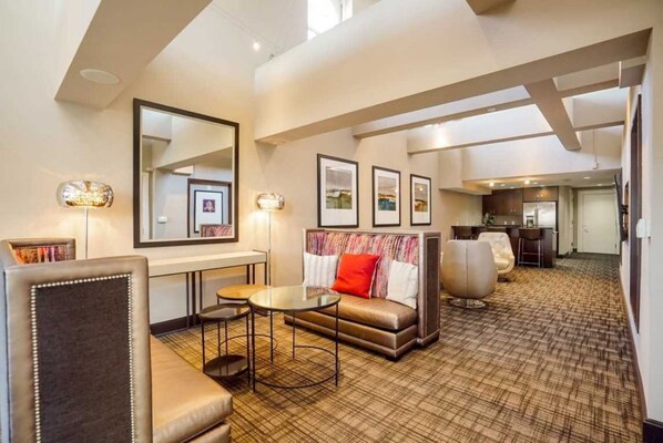 A modern hotel lobby with a sofa, armchairs, a coffee table, and framed pictures on the wall.