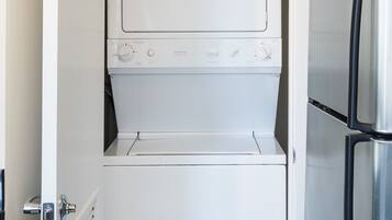 A compact laundry room with a white washer and dryer, a stainless steel refrigerator, and a wooden floor.
