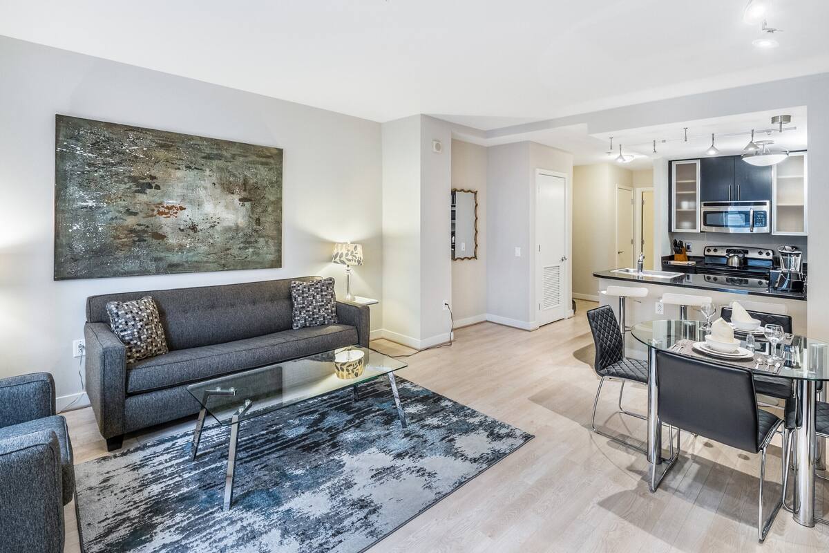 Ein modernes Wohnzimmer mit einem grauen Sofa, einem Glastisch und einem großen abstrakten Gemälde an der Wand.
