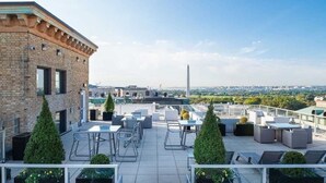 Een terras op het dak met buitenmeubilair, een uitzicht op de skyline van de stad en een opvallend monument in de verte.