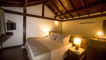 Une chambre avec un plafond en bois, un lit recouvert de draps blancs, deux lampes de chevet, une table de chevet et un climatiseur fixé au mur.