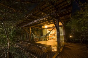 A wooden deck with a hammock and benches, leading to a building with a glass door and curtains. - Bupitanga Hotel (Tibau do Sul)