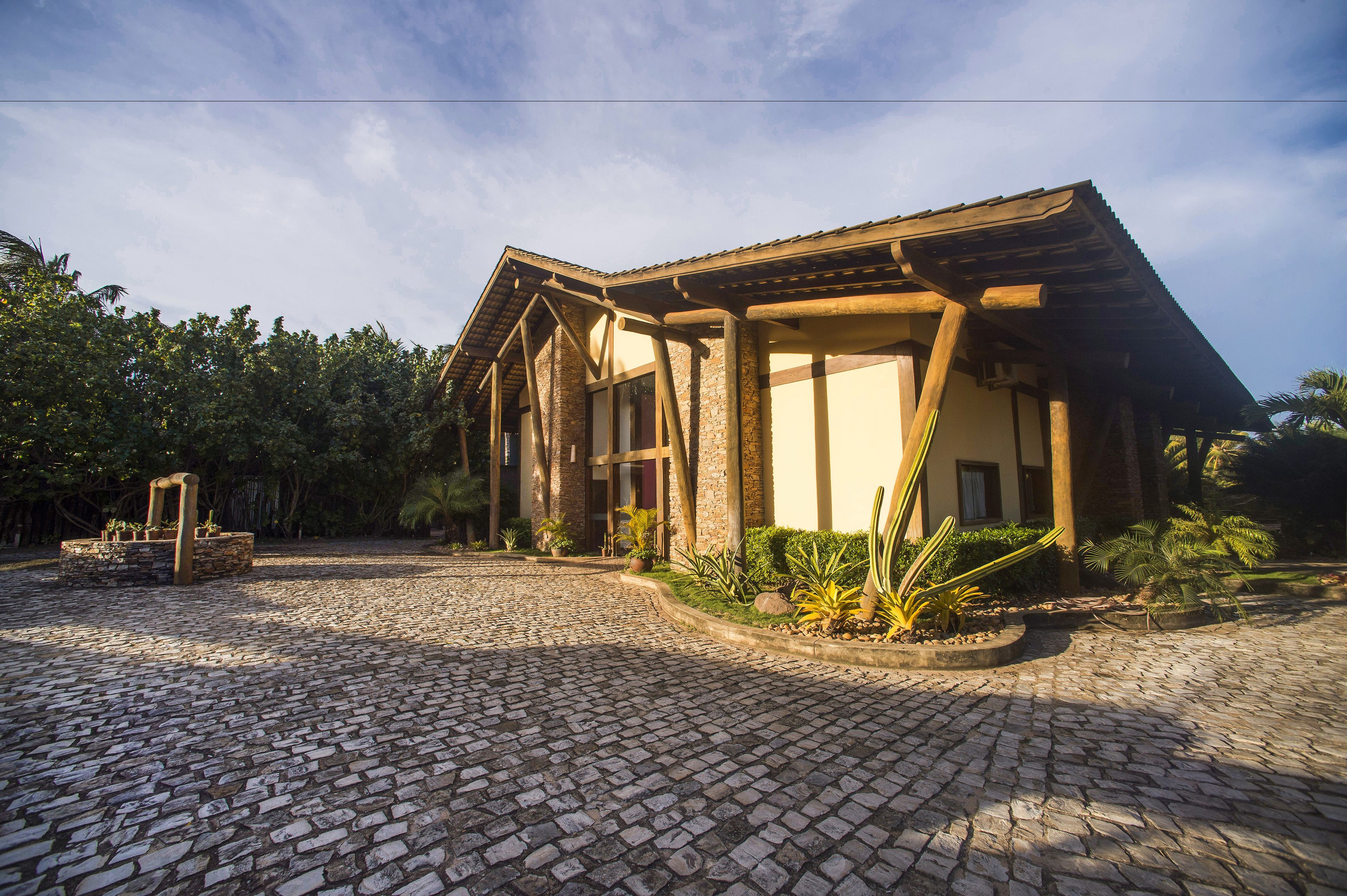 Un edificio con fachada de piedra y vigas de madera, rodeado por un patio empedrado y vegetación tropical.