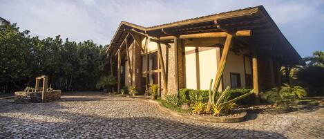 Un edificio con fachada de piedra y vigas de madera, rodeado por un patio empedrado y vegetación tropical.