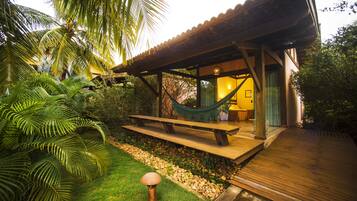 A wooden deck with a hammock and picnic table, surrounded by lush greenery and a palm tree.