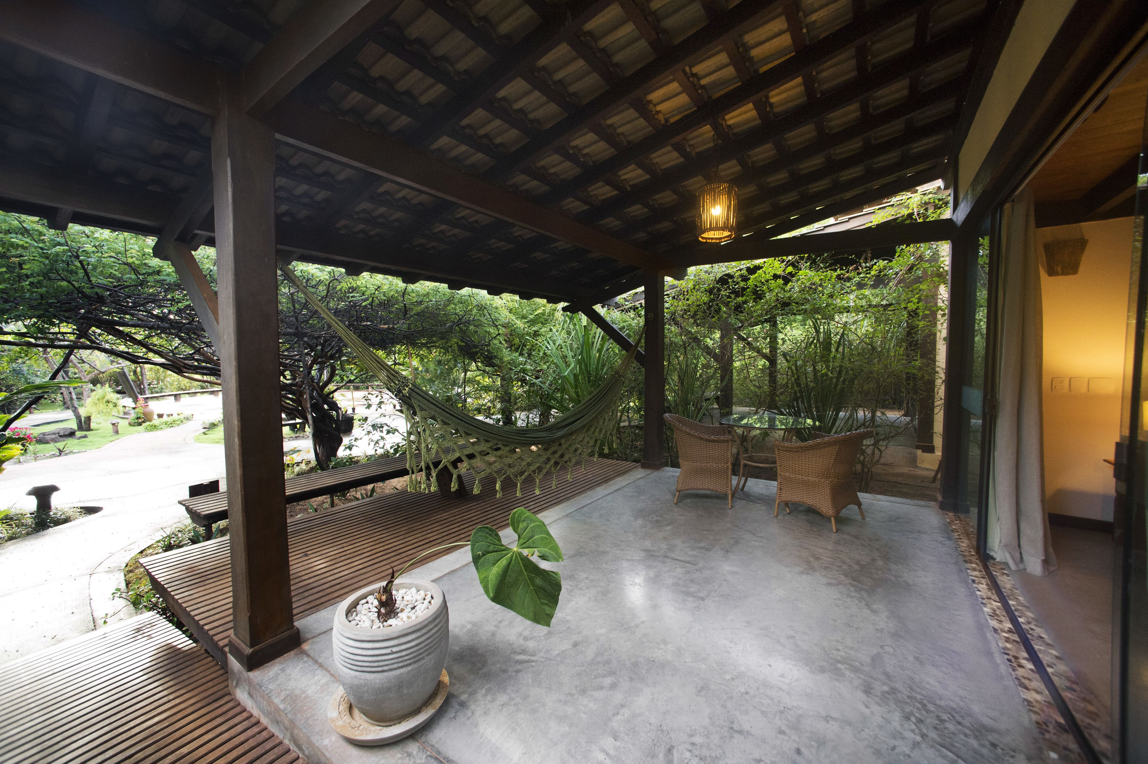 A covered outdoor area with a hammock, wicker furniture, and a potted plant.