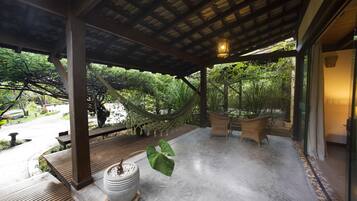 A covered outdoor area with a hammock, wicker furniture, and a potted plant.
