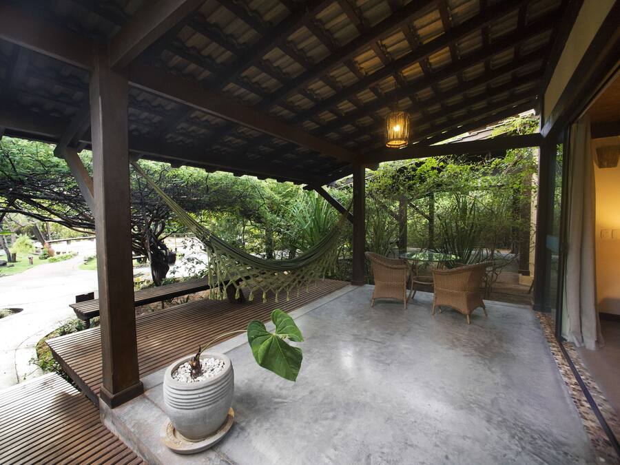A covered outdoor area with a hammock, wicker furniture, and a potted plant.