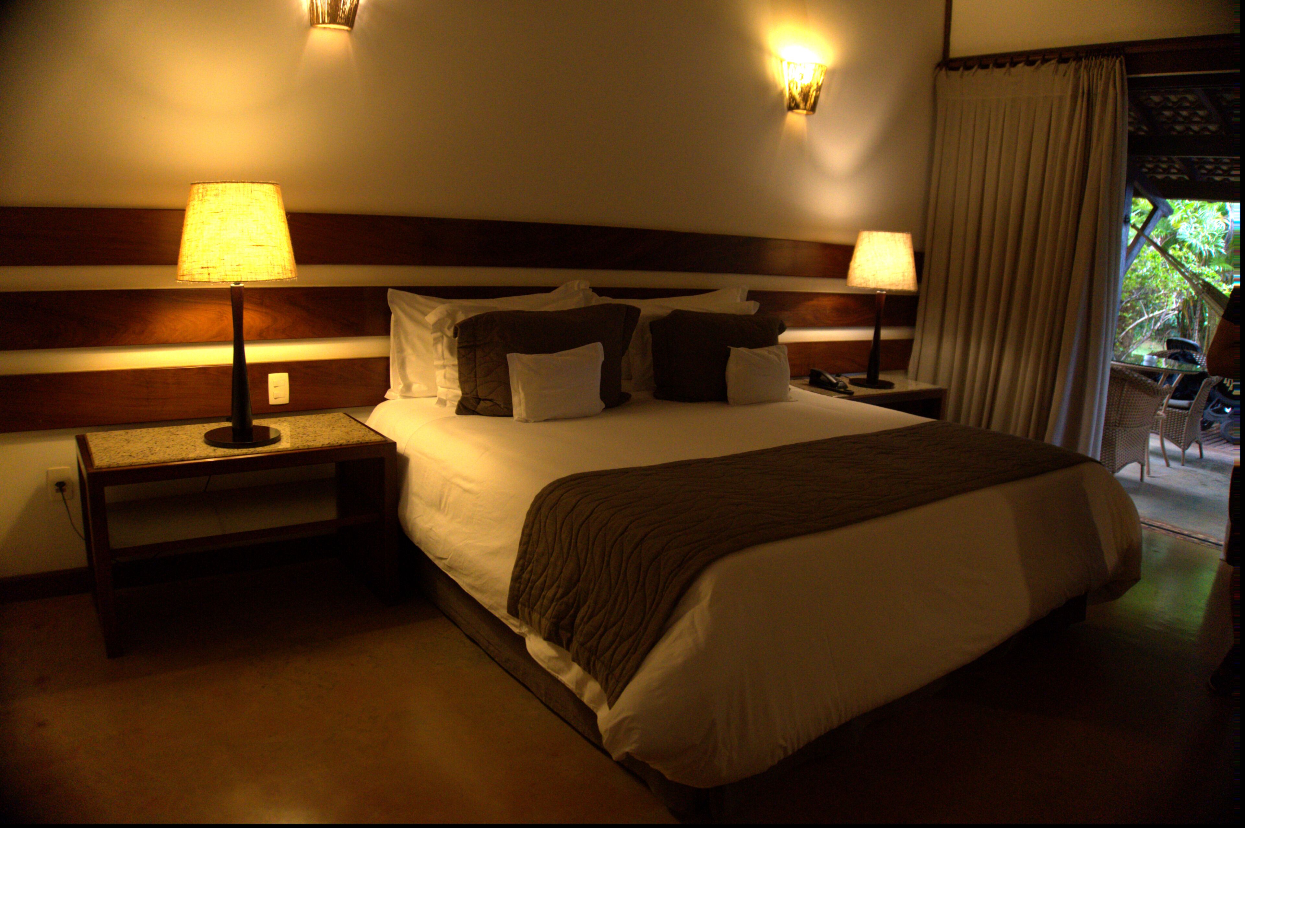 Een hotelkamer met een groot bed, twee bedlampen, een nachtkastje en uitzicht op het landschap door een raam.