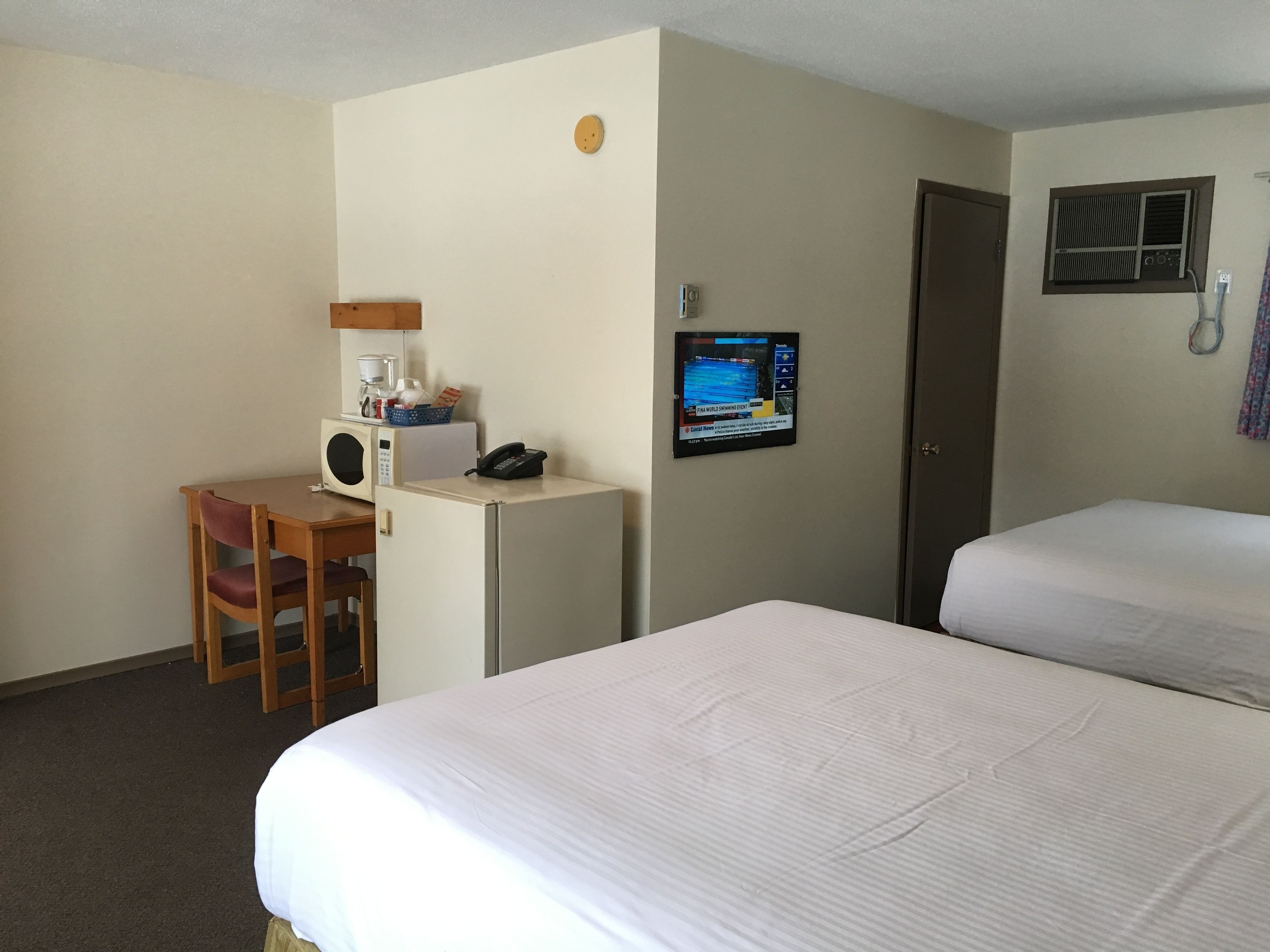 Une chambre d’hôtel avec deux lits, un bureau doté d’un micro-ondes, une chaise, un téléphone et un téléviseur fixé au mur.