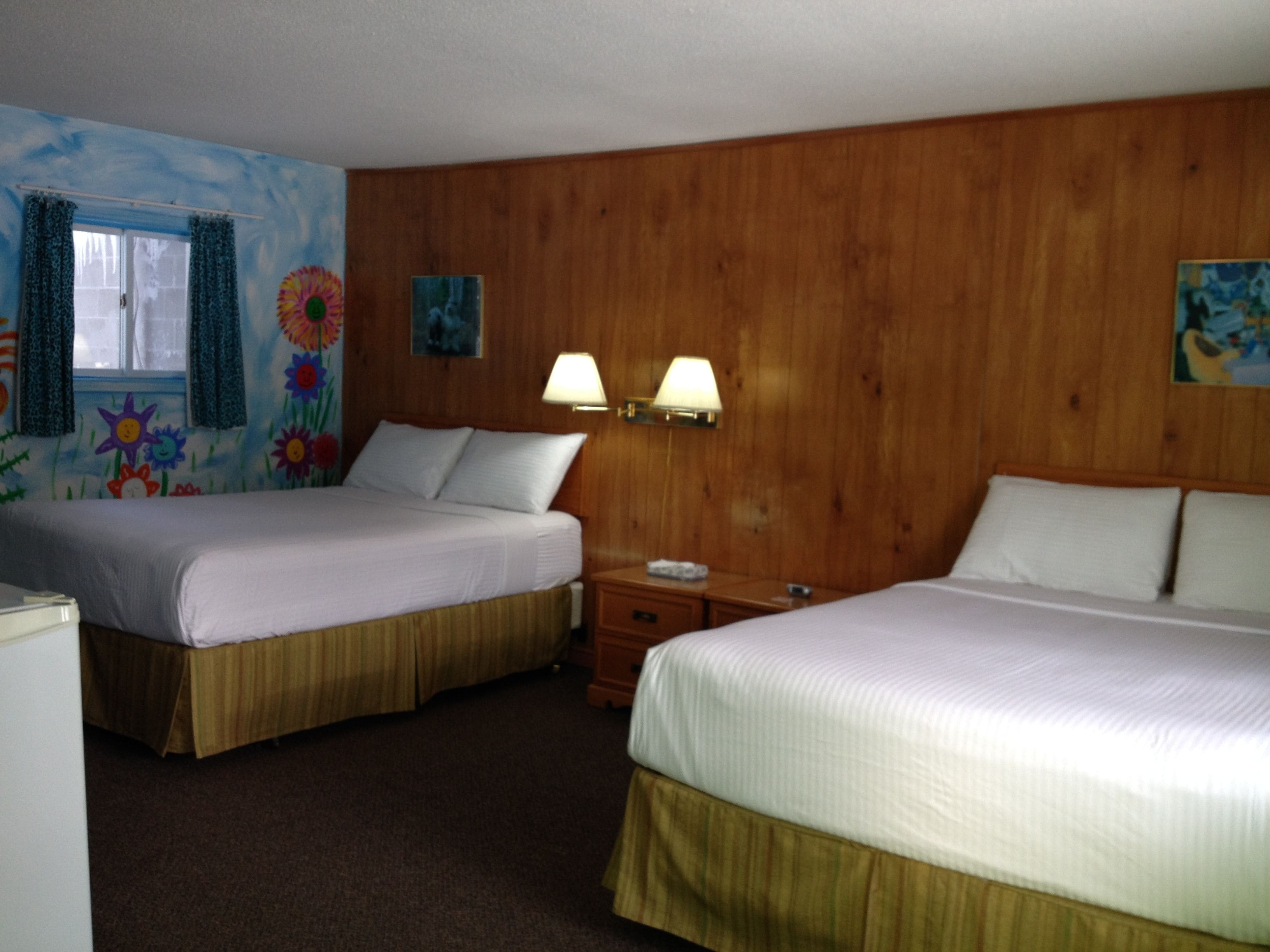 A hotel room with two beds, wooden paneling, a window with curtains, and wall art.