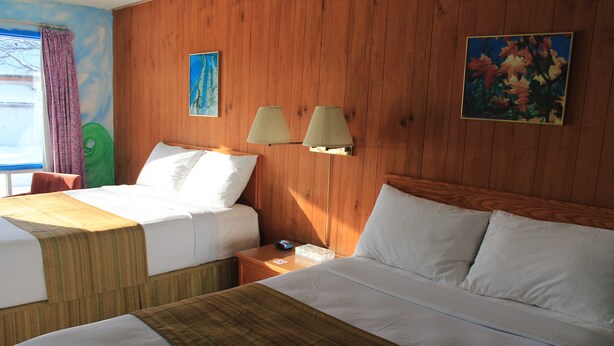 A hotel room with two beds, wooden paneling, a window with curtains, and two wall-mounted lamps. - Algonquin Motel (Machar)