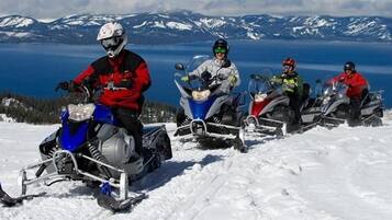 Cuatro motos de nieve en un paisaje nevado con un lago y montañas al fondo.