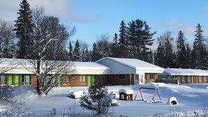 A snow-covered building with multiple rooms, surrounded by trees and a snowy landscape. - Algonquin Motel (Machar)
