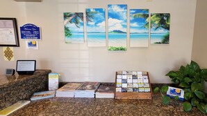 A reception desk with a check-in counter, framed welcome sign, and a wall with tropical beach paintings. - Pismo Beachwalker Inn & Suites (Pismo Beach)