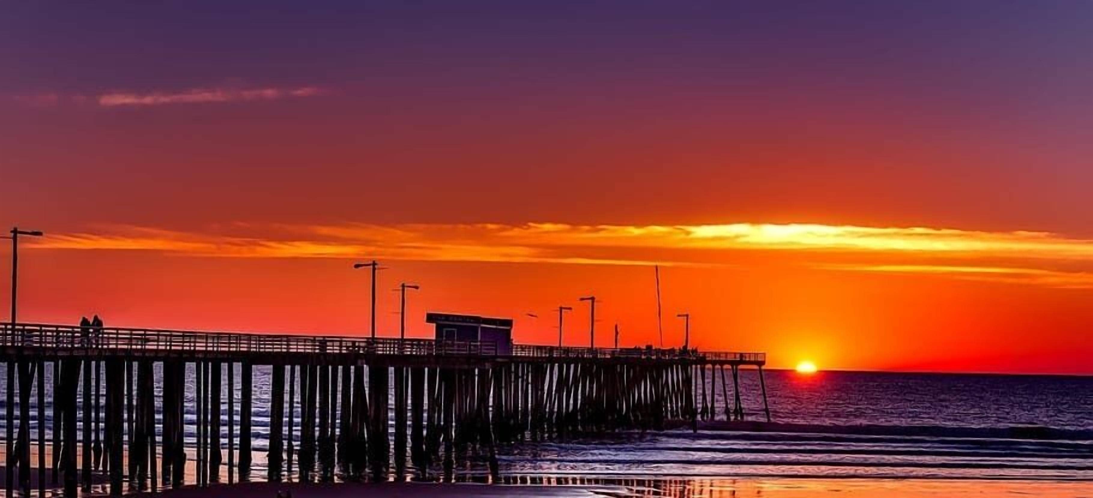 A pier extending into the ocean with a sunset in the background.