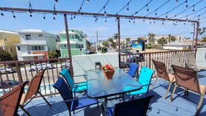 A balcony with a glass table and chairs, a flower pot, and a view of buildings and palm trees. - Pismo Beachwalker Inn & Suites (Pismo Beach)