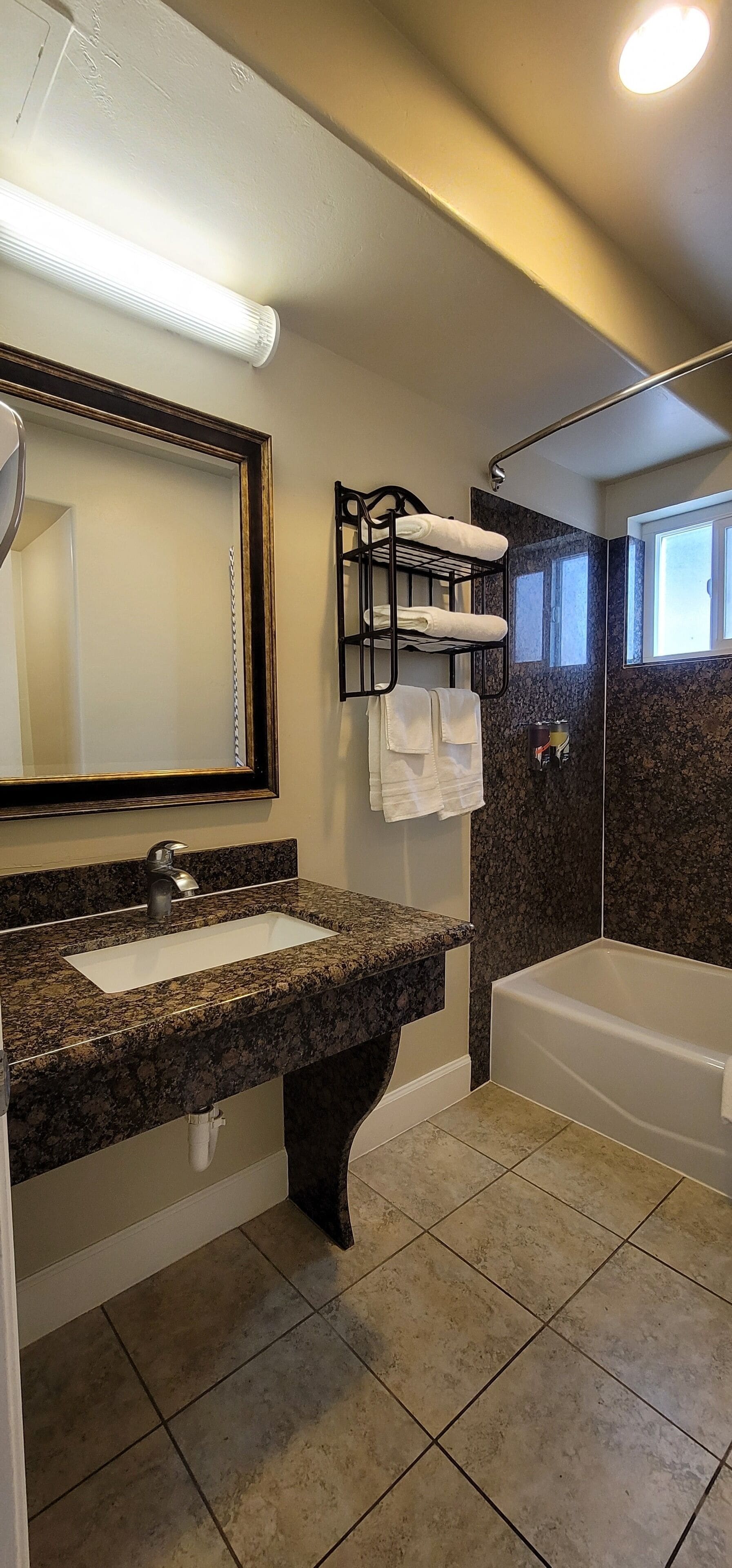 A bathroom with a granite countertop sink, a large mirror, a black towel rack, a shower, and a bathtub.