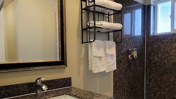 A bathroom with a granite countertop sink, a large mirror, a black towel rack, a shower, and a bathtub.