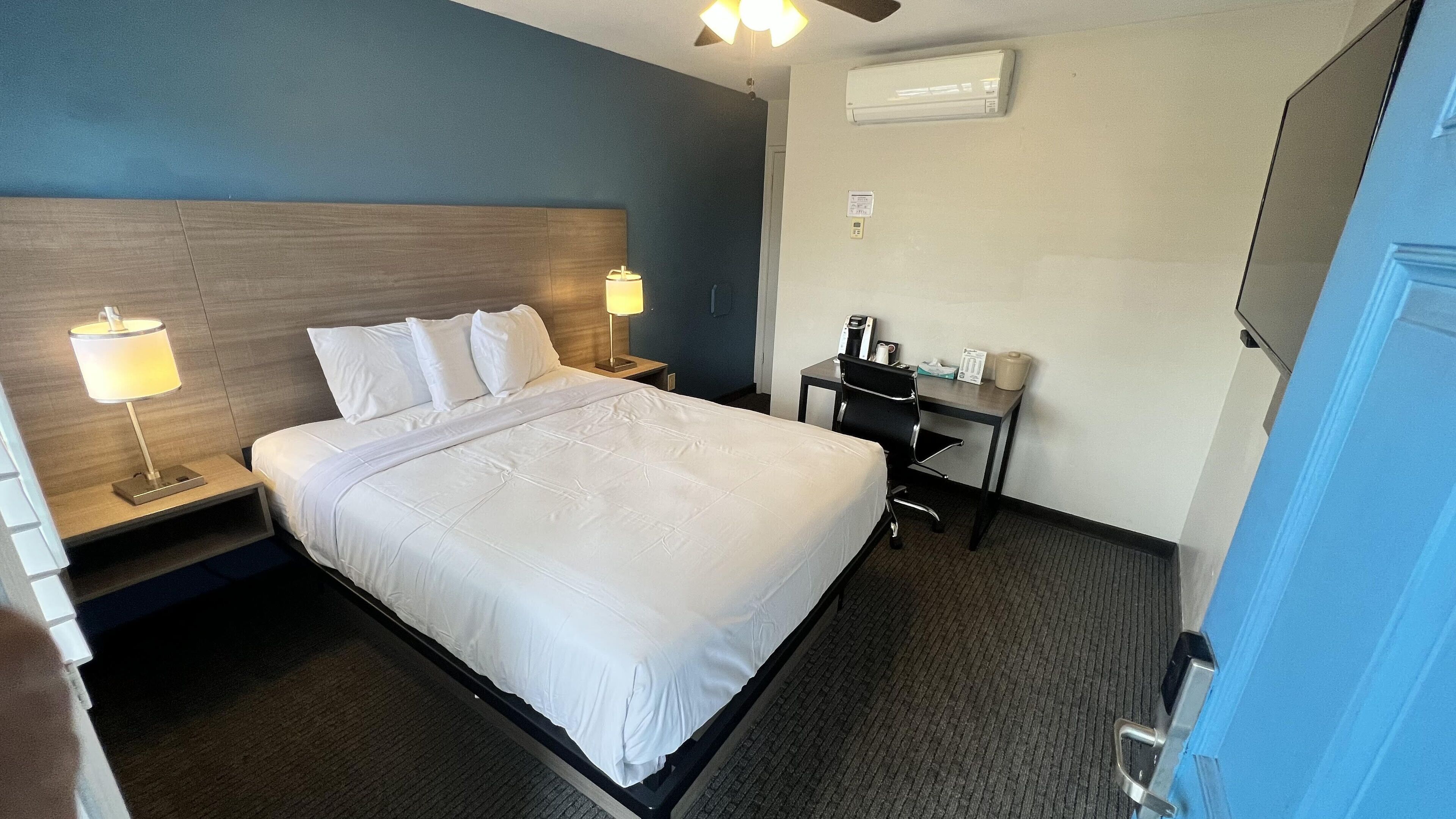 Habitación de hotel con cama, lámparas de noche, escritorio con silla y un equipo de aire acondicionado en la pared.