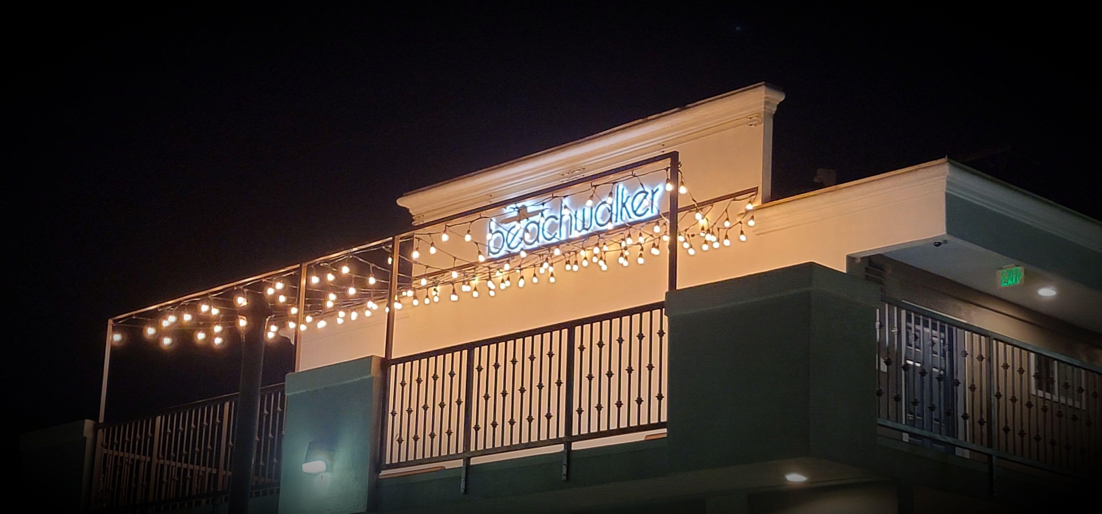 A building with a neon sign reading "beachwalker" and string lights above the entrance.
