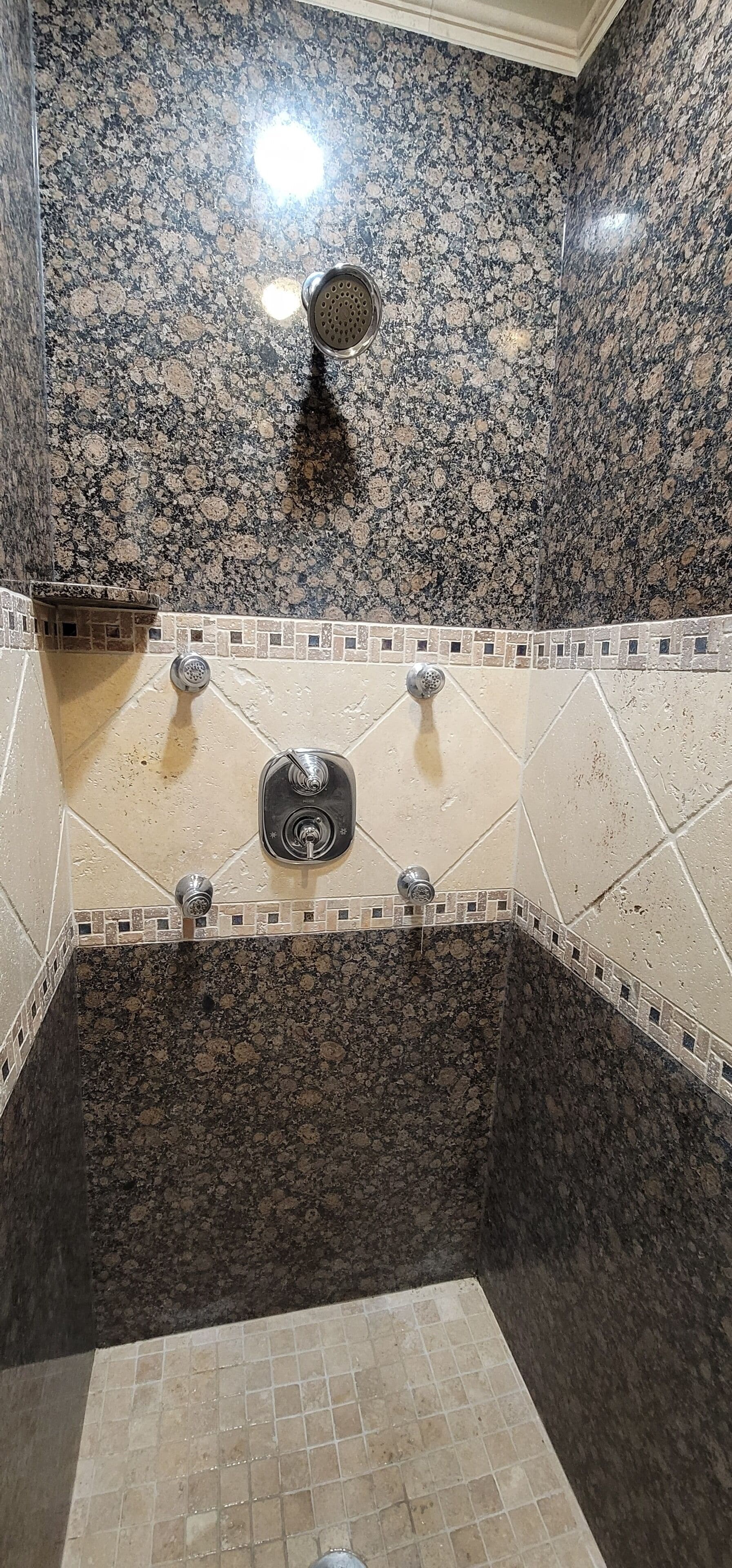 A bathroom with a granite shower wall, a tiled floor, and a central sink with a faucet.