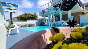 A hotel pool area with lounge chairs, a sign for 'Beachwalker Inn & Suites', and a flower bed. - Pismo Beachwalker Inn & Suites (Pismo Beach)