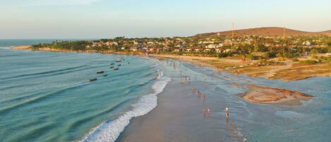 Un pueblo costero con una playa, barcos y una colina al fondo.