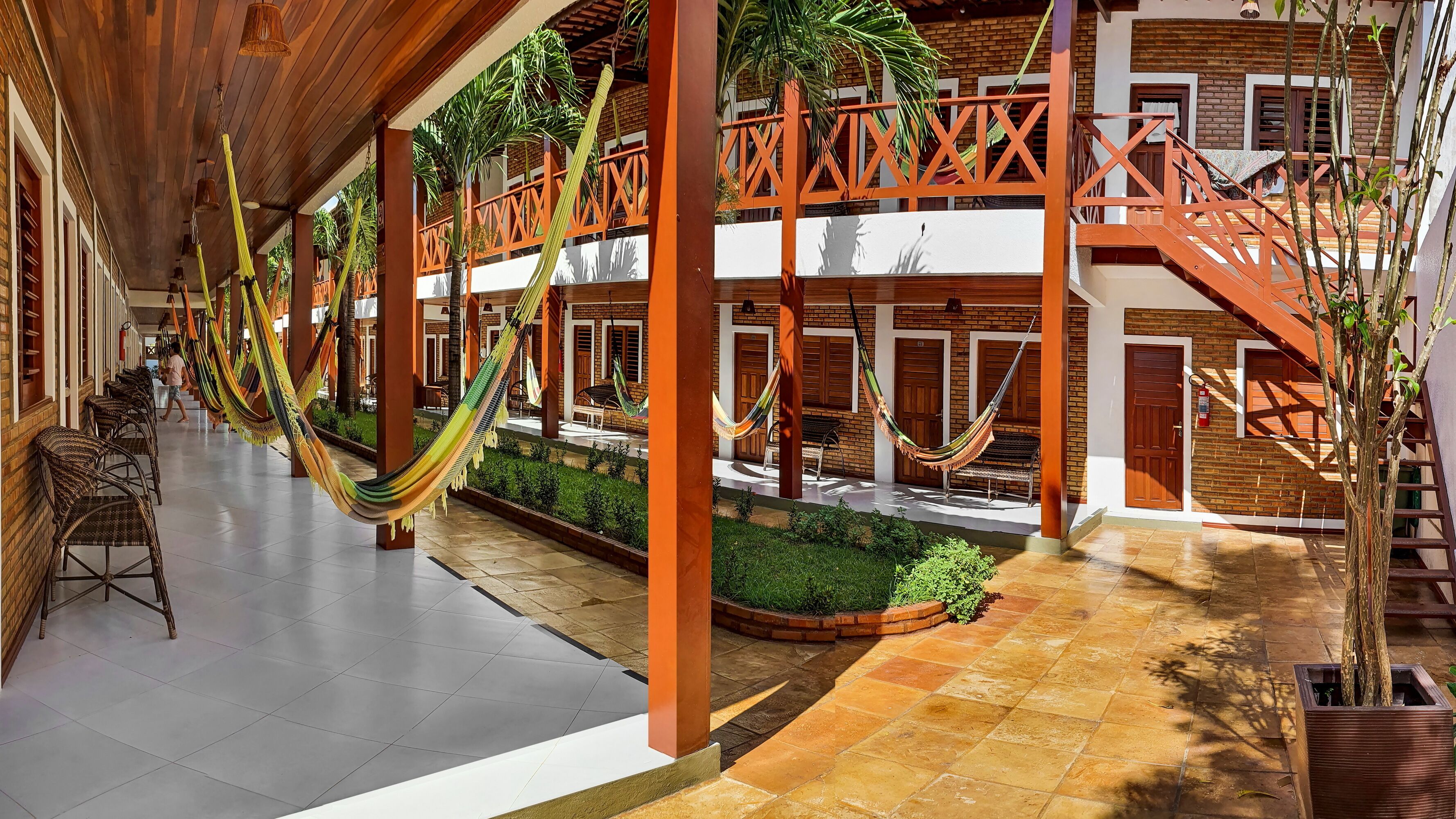 A spacious courtyard with hammocks, a covered seating area, and a brick building with wooden doors.
