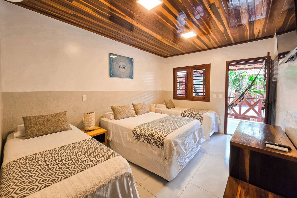 A hotel room with two beds, wooden ceiling, a window with shutters, and a sign on the wall.