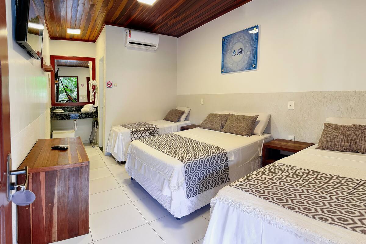 A hotel room with two beds, a wooden desk, a mirror, and a wall-mounted air conditioner.