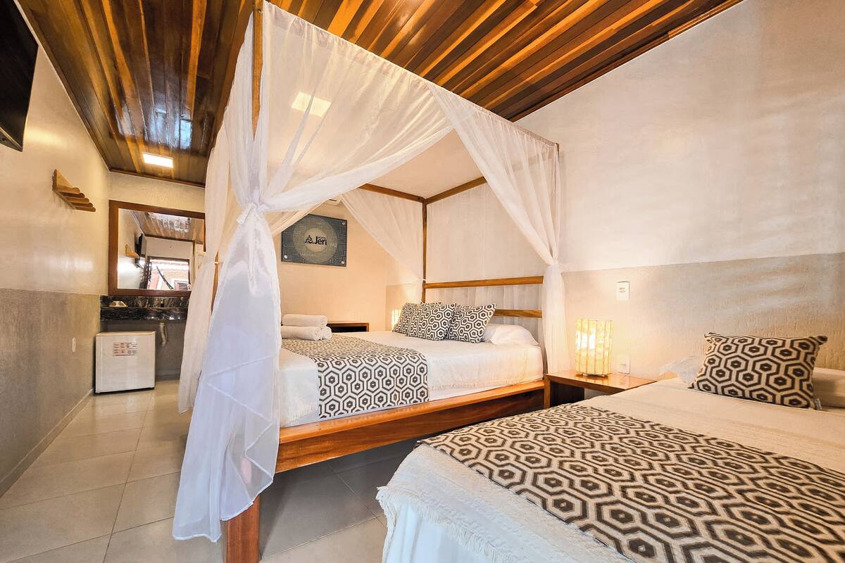 A bedroom with two beds, a wooden ceiling, a small kitchenette, and a mirror.