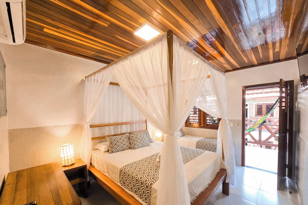 A bedroom with a wooden ceiling, a bed with a canopy, a bedside table, and a remote control on the table.