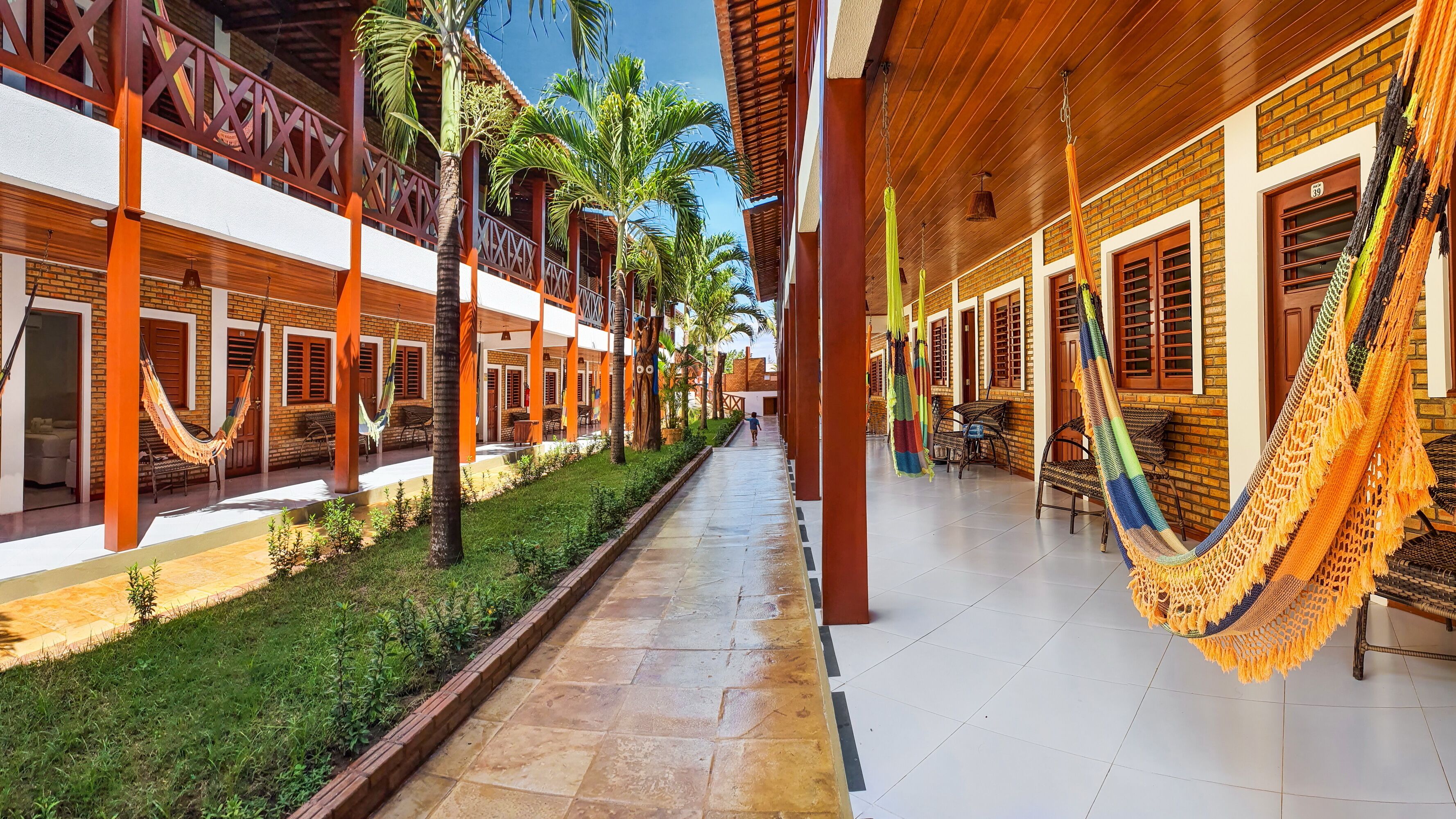 A hotel corridor with hammocks, palm trees, and a tiled walkway.