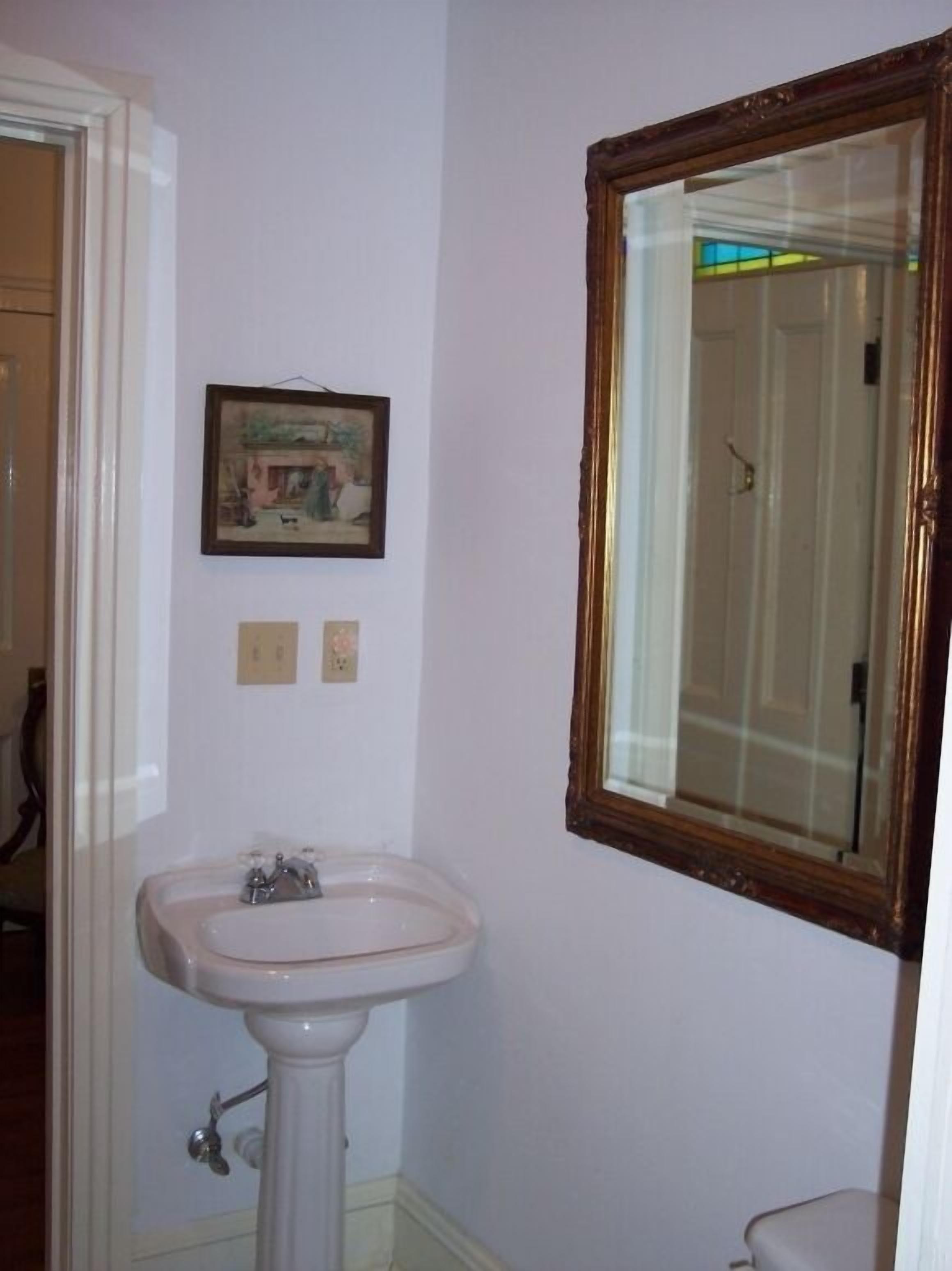 Un bany amb un lavabo sobre pèdia, un mirall emmarcat i un quadre penjat a la paret.