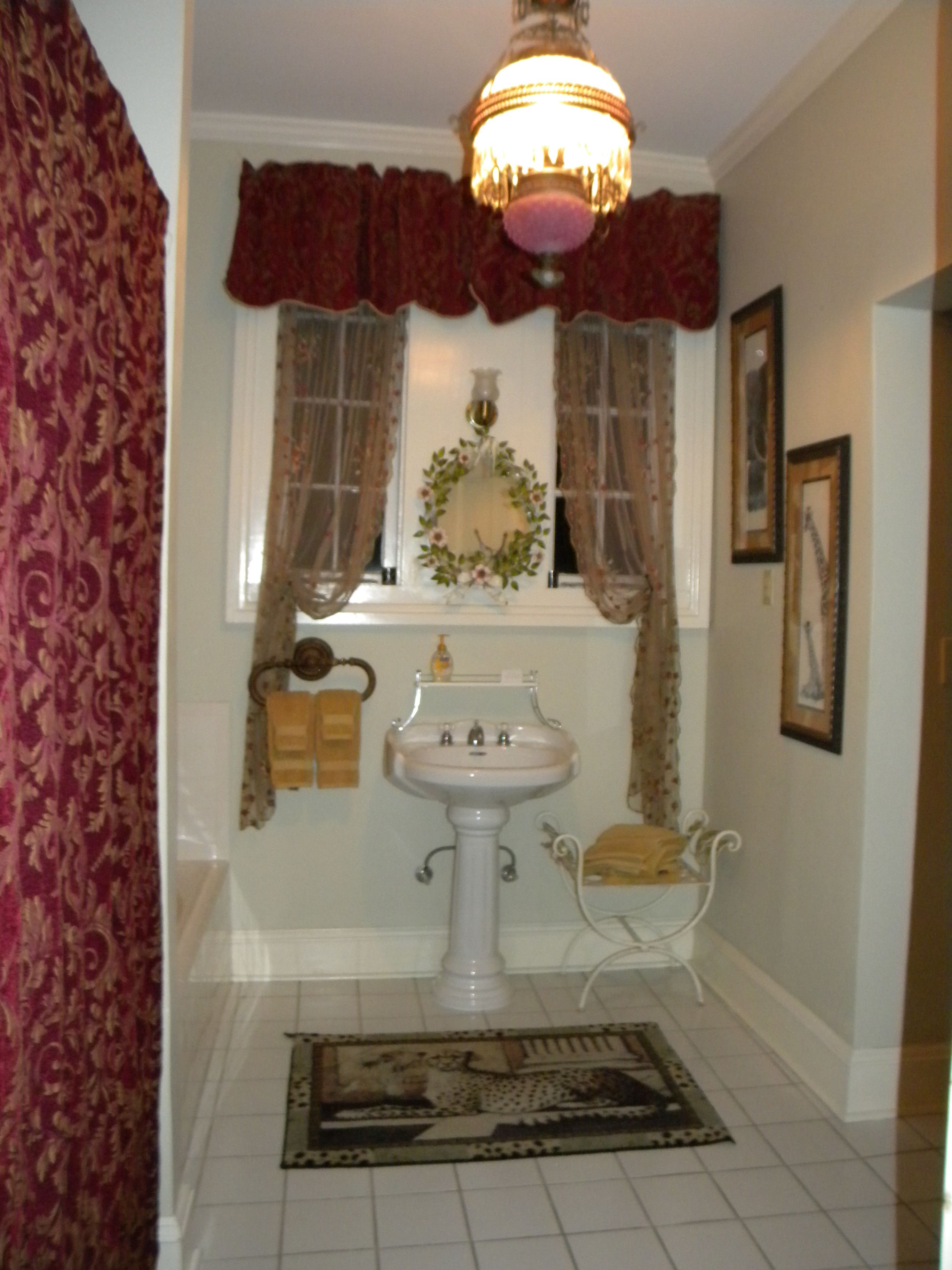A bathroom with a pedestal sink, a decorative wreath on the window, and a leopard print rug on the floor.
