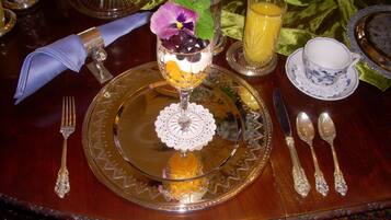 Una mesa de comedor formal con una copa de postre, un mantelino azul y una guarnición de frutas.