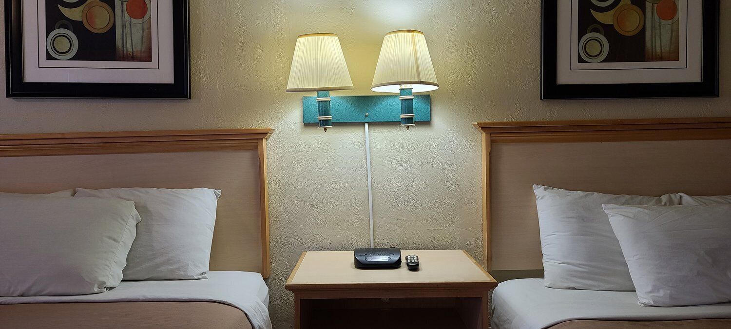 A hotel room with two beds, a nightstand with a lamp, and artwork on the walls.